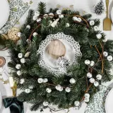 Un centre de table Noël nature avec une couronne de sapin, des clochettes blanches et des éléments décoratifs rustiques.