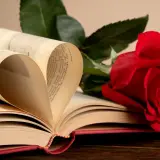 Un livre ouvert forme un cœur avec ses pages. Une rose rouge repose à côté, symbolisant l'amour et la passion. Que signifie la rose ? L'amour éternel, peut-être.