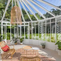 Une petite véranda cosy avec des meubles en rotin, des plantes vertes et une grande suspension en osier. Parfait pour un coin lecture paisible.