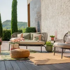 Aménagement terrasse extérieure : un canapé et un fauteuil confortables, des coussins, des plaids et des plantes créent un espace détente accueillant.