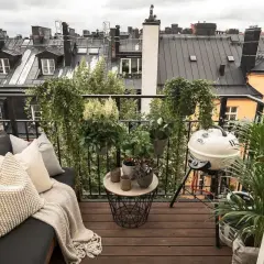 Aménagement terrasse appartement : un coin salon confortable avec coussins, une table basse, un barbecue et de nombreuses plantes, offrant une vue sur les toits.