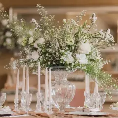 Une élégante composition florale blanche trône sur une table dressée, entourée de bougies fines et de verres ciselés.