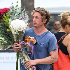 Un homme porte un bouquet de fleurs et une peluche de faon. Offrir des fleurs à un homme, signification : un geste d'affection ou de reconnaissance.