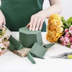Préparation d'un bouquet : on coupe la mousse pour piquer des fleurs, entourée de roses jaunes et roses.