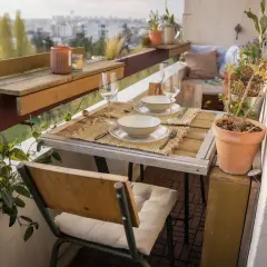 Jolie deco balcon avec table dressée pour deux, plantes vertes et vue sur la ville. Parfait pour un dîner romantique.