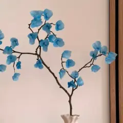 Une branche décorative avec des fleurs bleues en papier, une composition florale à faire soi-même.