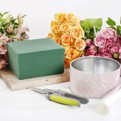 Préparation d'une petite composition florale simple : roses roses et jaunes, alstroemérias, mousse florale, boîte, ciseaux et film.