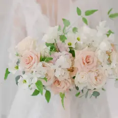 Un bouquet de mariée tombant original, composé de roses douces et de fleurs blanches délicates, drapé sur une robe de mariée.