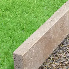 Une bordure en béton beige, posée sur des graviers, délimite une pelouse verte.