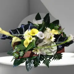 Composition florale élégante avec des arums blancs et jaunes, des feuillages sombres et des petites fleurs blanches.
