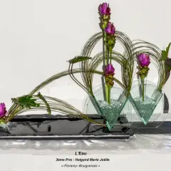 Composition florale en hauteur avec des fleurs roses et des feuillages verts, dans des vases en verre triangulaires.
