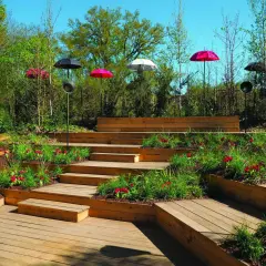Aménagement d'une butte de terre en pente avec des terrasses en bois, des tulipes rouges et des parasols colorés.