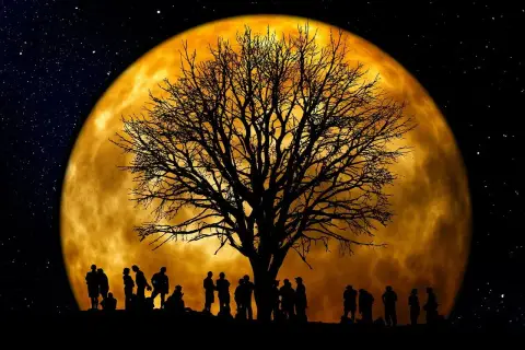 Silhouettes de personnes sous un arbre nu, devant une immense lune orangée. Une scène mystique pour jardiner avec la lune.
