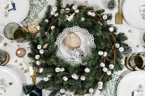 Un centre de table Noël nature avec une couronne de sapin, des clochettes blanches et des éléments décoratifs rustiques.