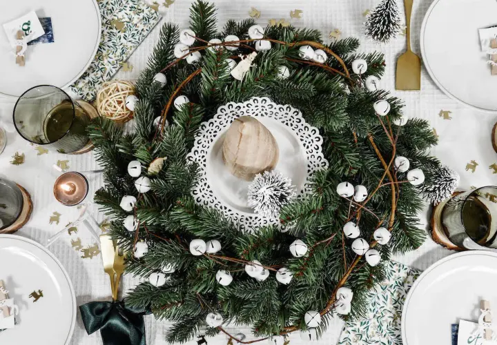 Un centre de table Noël nature avec une couronne de sapin, des clochettes blanches et des éléments décoratifs rustiques.