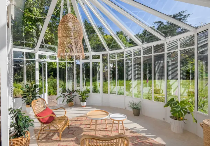 Une petite véranda cosy avec des meubles en rotin, des plantes vertes et une grande suspension en osier. Parfait pour un coin lecture paisible.