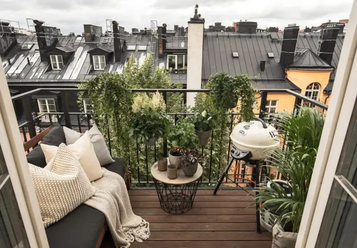 Aménagement terrasse appartement : un coin salon confortable avec coussins, une table basse, un barbecue et de nombreuses plantes, offrant une vue sur les toits.