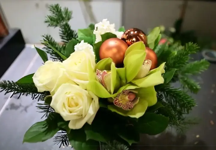 Un magnifique bouquet de noël à faire soi-même avec roses blanches, orchidées vertes, boules cuivrées et branches de sapin.
