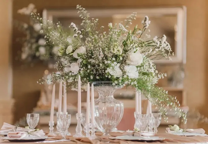 Une élégante composition florale blanche trône sur une table dressée, entourée de bougies fines et de verres ciselés.