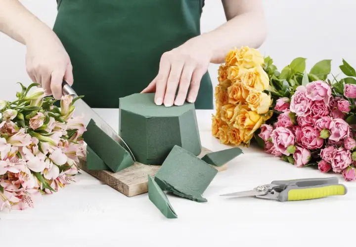 Préparation d'un bouquet : on coupe la mousse pour piquer des fleurs, entourée de roses jaunes et roses.