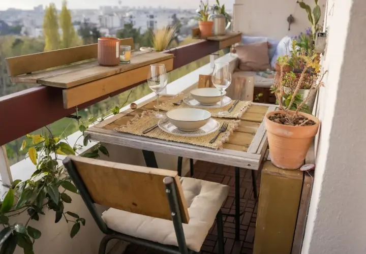 Jolie deco balcon avec table dressée pour deux, plantes vertes et vue sur la ville. Parfait pour un dîner romantique.