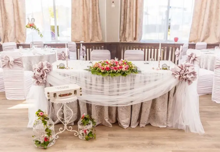 Magnifique table de mariage champêtre ornée de fleurs roses et blanches, de voilages légers et de cages décoratives.