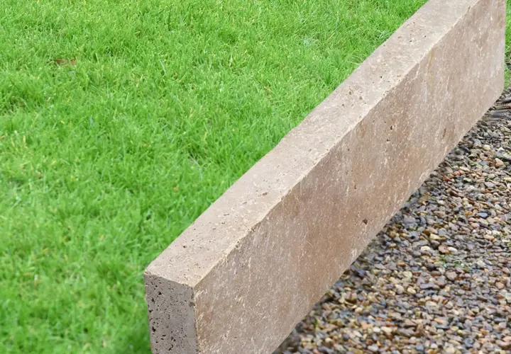 Une bordure en béton beige, posée sur des graviers, délimite une pelouse verte.