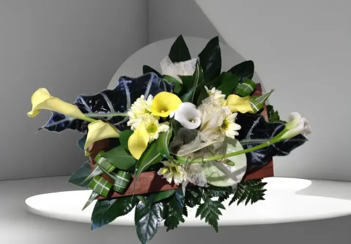 Composition florale élégante avec des arums blancs et jaunes, des feuillages sombres et des petites fleurs blanches.