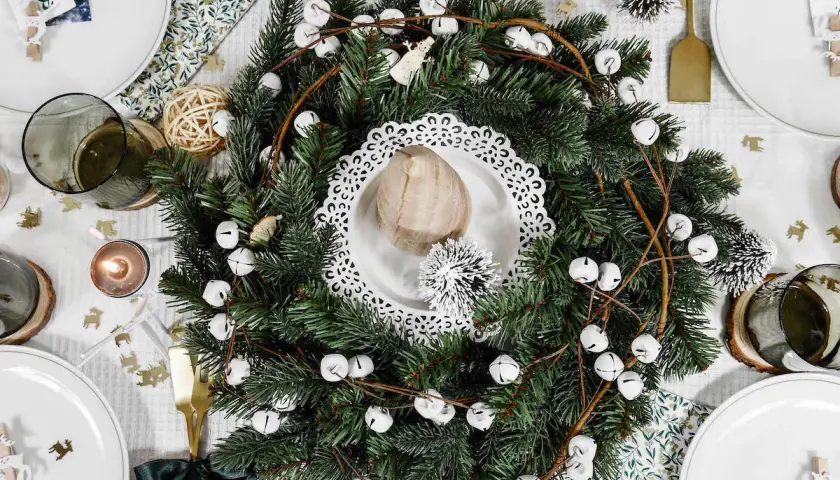 Un centre de table Noël nature avec une couronne de sapin, des clochettes blanches et des éléments décoratifs rustiques.