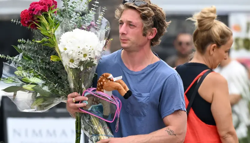 Un homme porte un bouquet de fleurs et une peluche de faon. Offrir des fleurs à un homme, signification : un geste d'affection ou de reconnaissance.