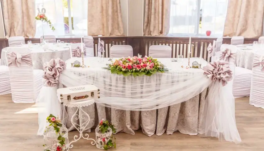 Magnifique table de mariage champêtre ornée de fleurs roses et blanches, de voilages légers et de cages décoratives.