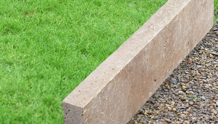 Une bordure en béton beige, posée sur des graviers, délimite une pelouse verte.