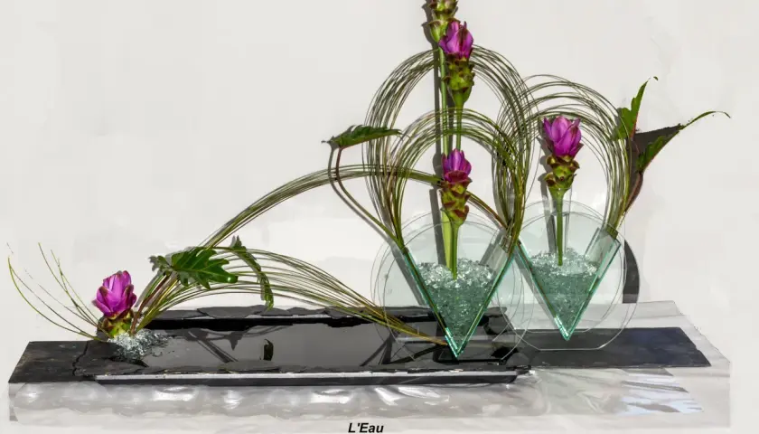 Composition florale en hauteur avec des fleurs roses et des feuillages verts, dans des vases en verre triangulaires.