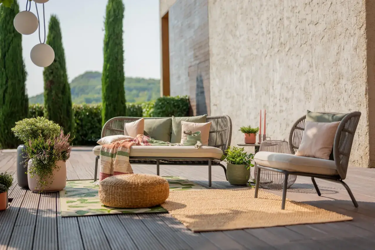 Aménagement terrasse extérieure : un canapé et un fauteuil confortables, des coussins, des plaids et des plantes créent un espace détente accueillant.
