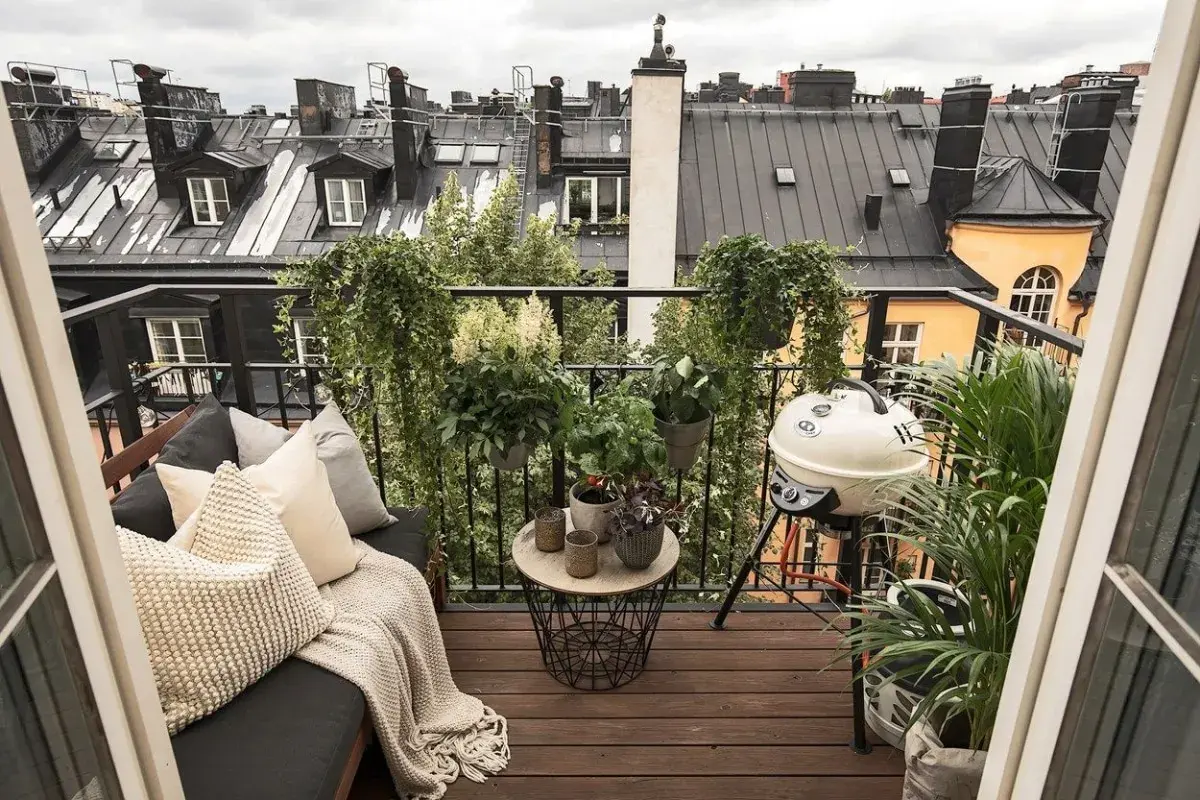 Aménagement terrasse appartement : un coin salon confortable avec coussins, une table basse, un barbecue et de nombreuses plantes, offrant une vue sur les toits.