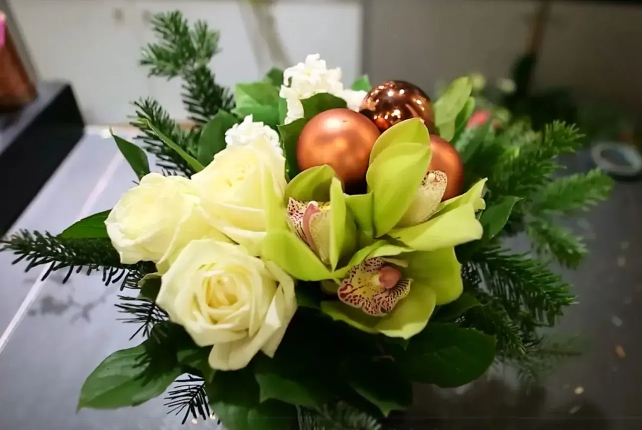 Un magnifique bouquet de noël à faire soi-même avec roses blanches, orchidées vertes, boules cuivrées et branches de sapin.