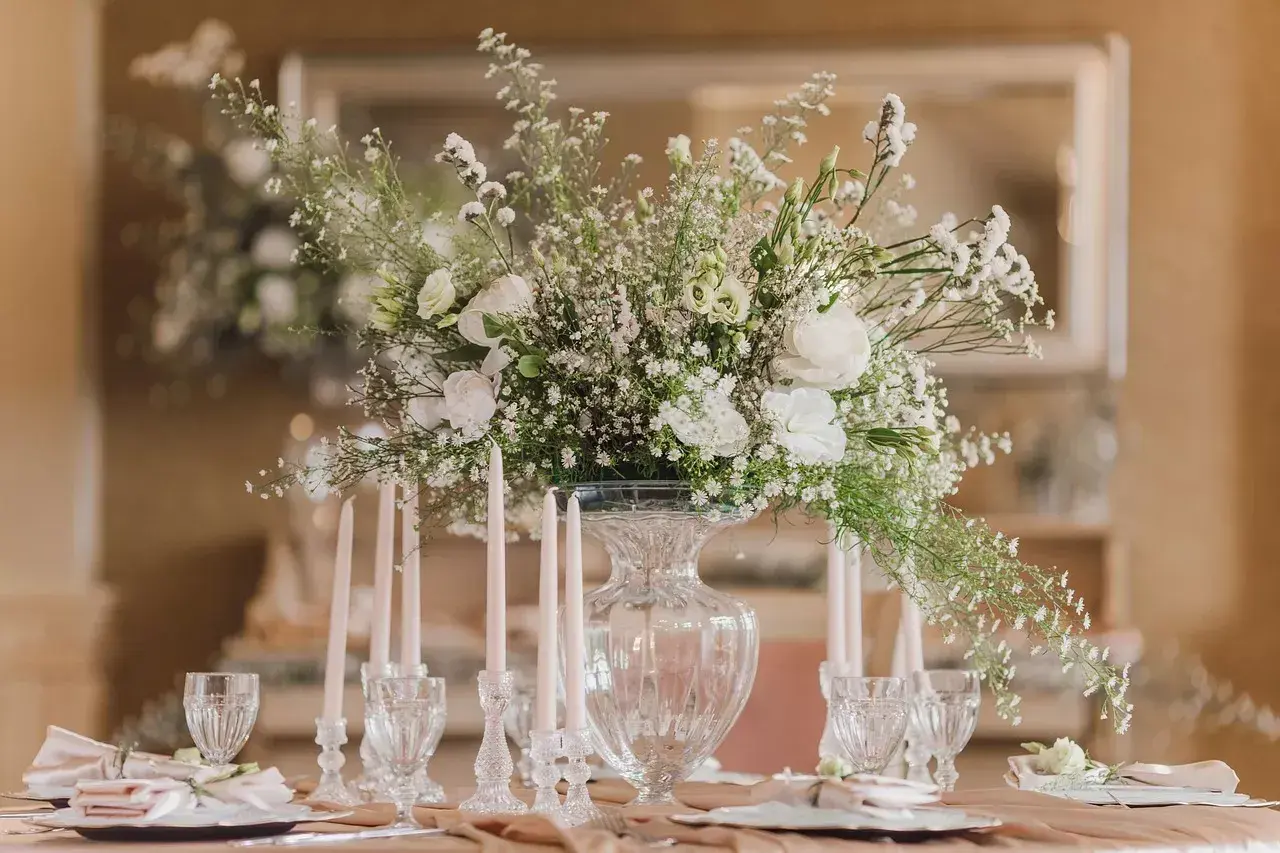 Une élégante composition florale blanche trône sur une table dressée, entourée de bougies fines et de verres ciselés.