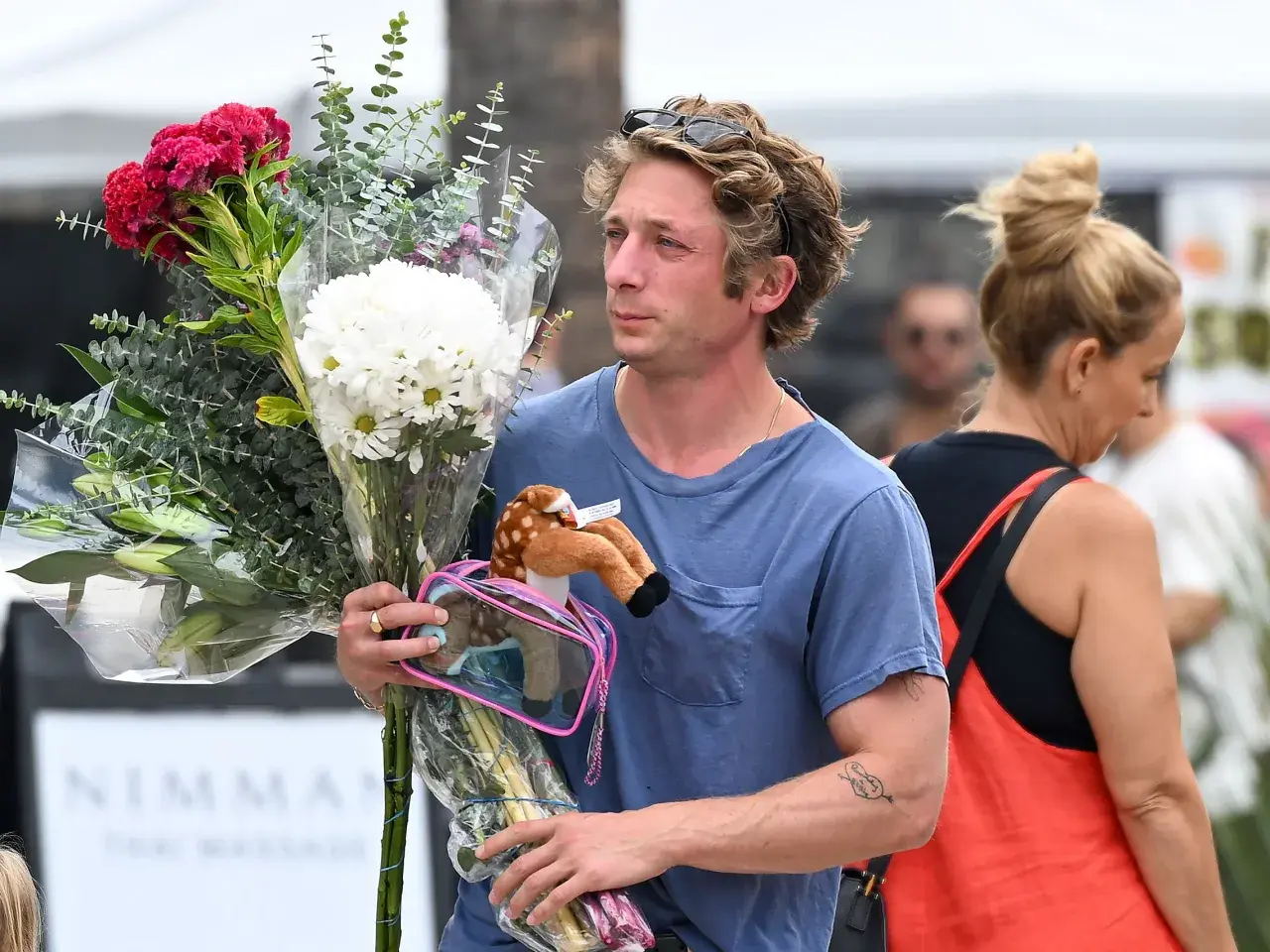 Un homme porte un bouquet de fleurs et une peluche de faon. Offrir des fleurs à un homme, signification : un geste d'affection ou de reconnaissance.