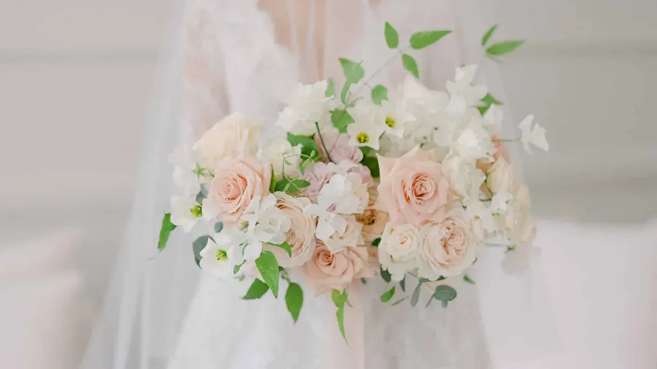Un bouquet de mariée tombant original, composé de roses douces et de fleurs blanches délicates, drapé sur une robe de mariée.