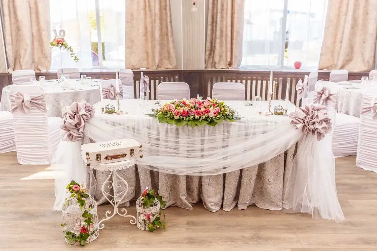 Magnifique table de mariage champêtre ornée de fleurs roses et blanches, de voilages légers et de cages décoratives.