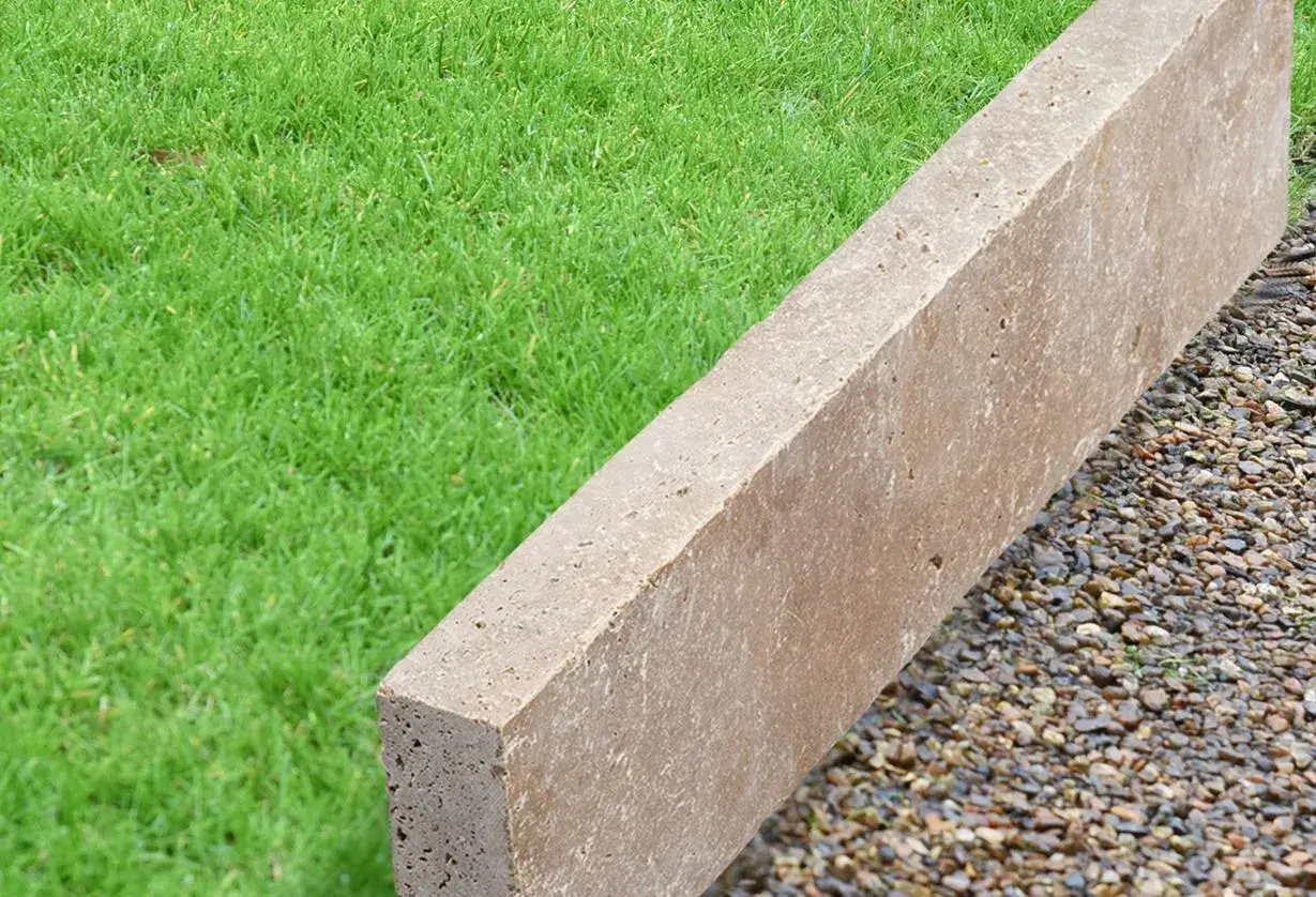 Une bordure en béton beige, posée sur des graviers, délimite une pelouse verte.