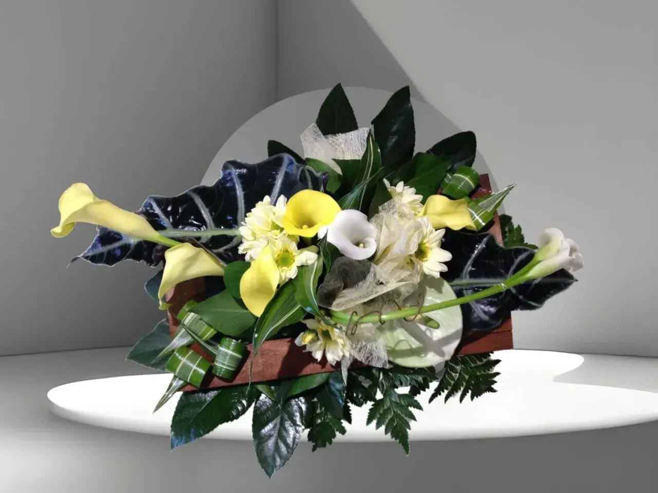 Composition florale élégante avec des arums blancs et jaunes, des feuillages sombres et des petites fleurs blanches.