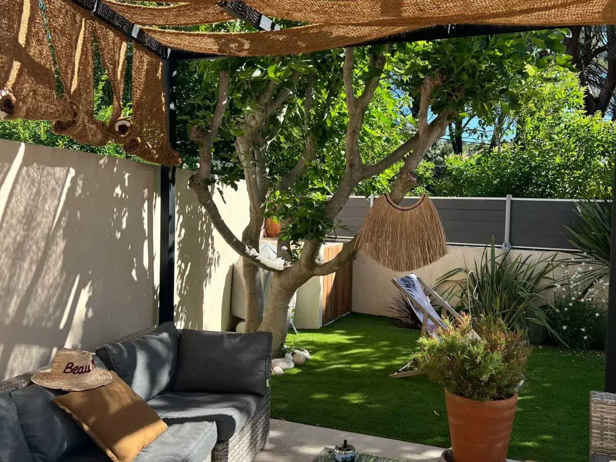 Aménager un petit jardin de 10m2 : salon de jardin confortable, fausse pelouse, arbre fruitier, paillasson décoratif et transat pour un coin détente.