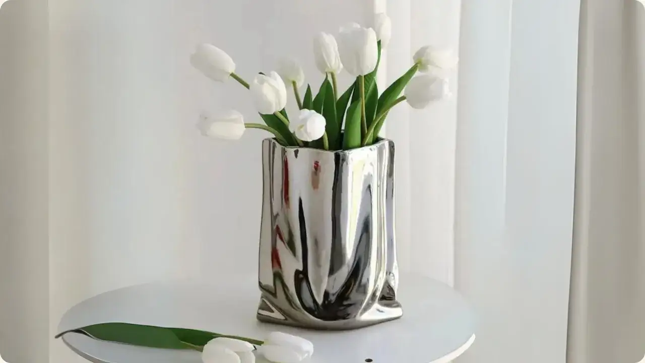 Un bouquet de tulipe ouverte blanche dans un vase argent&eacute;, sur une table blanche.