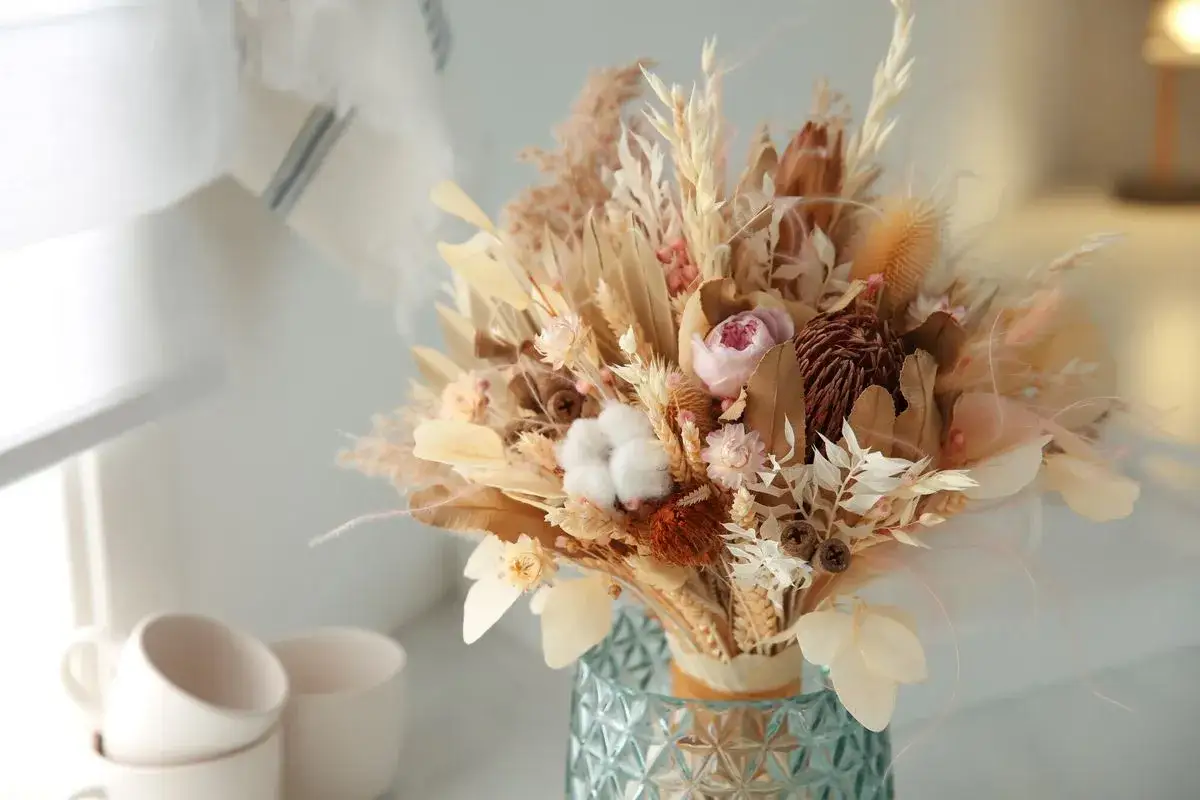 Un bouquet de fleurs séchées, dont certaines ont été conservées en utilisant la technique de faire sécher des fleurs avec du sel, dans un vase texturé.