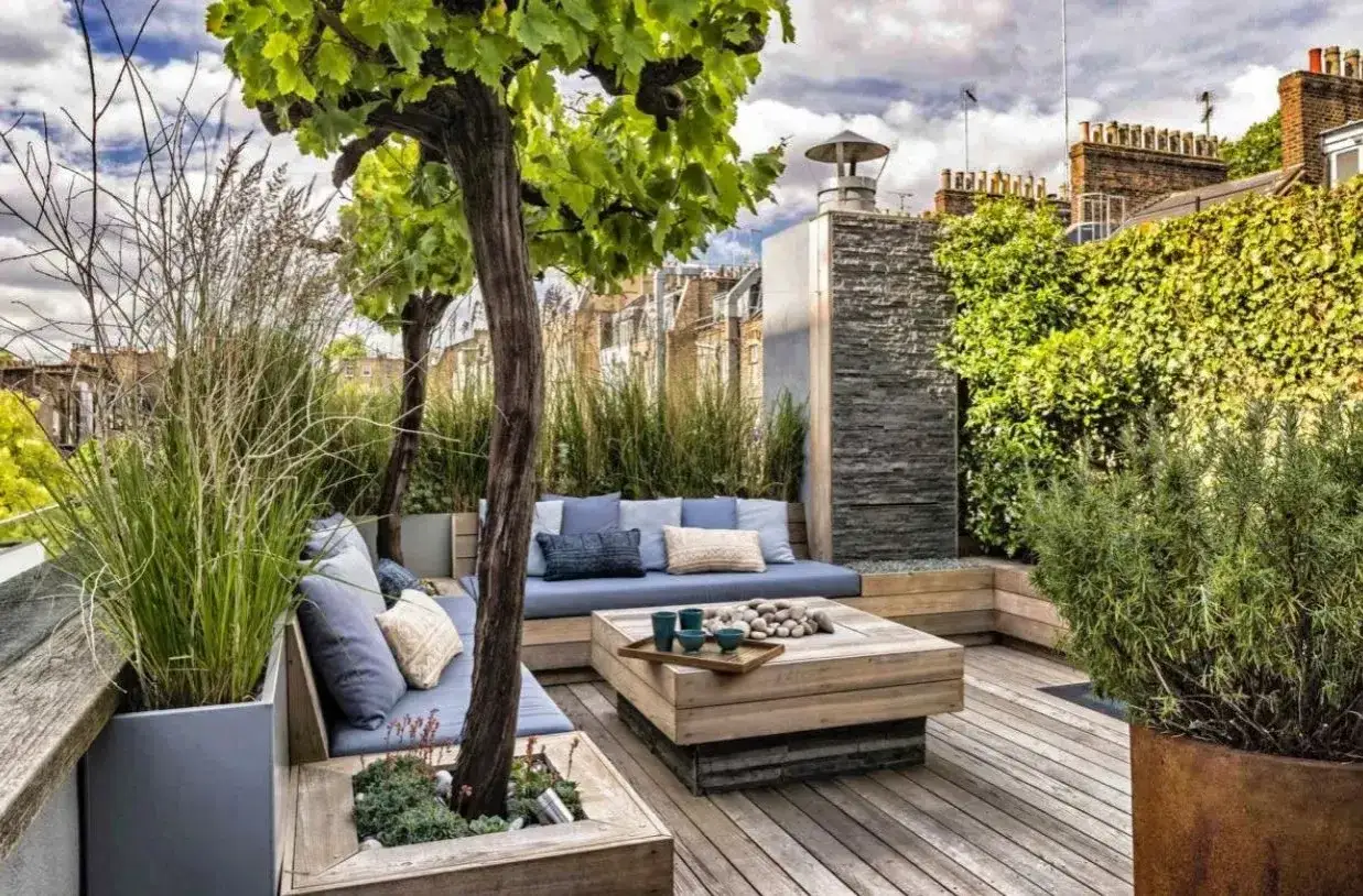 Am&eacute;nagement terrasse appartement avec banquette bleue, table basse en bois et v&eacute;g&eacute;tation luxuriante. Un coin d&eacute;tente chic et verdoyant.