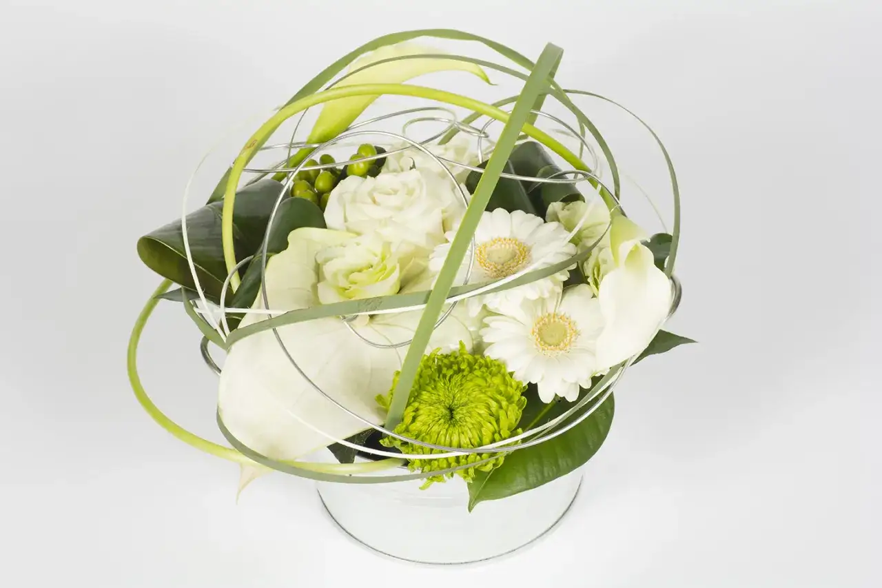 Composition florale ronde aux roses blanches, gerberas, callas et chrysanth&egrave;me vert, orn&eacute;e de fils m&eacute;talliques et de feuillage.