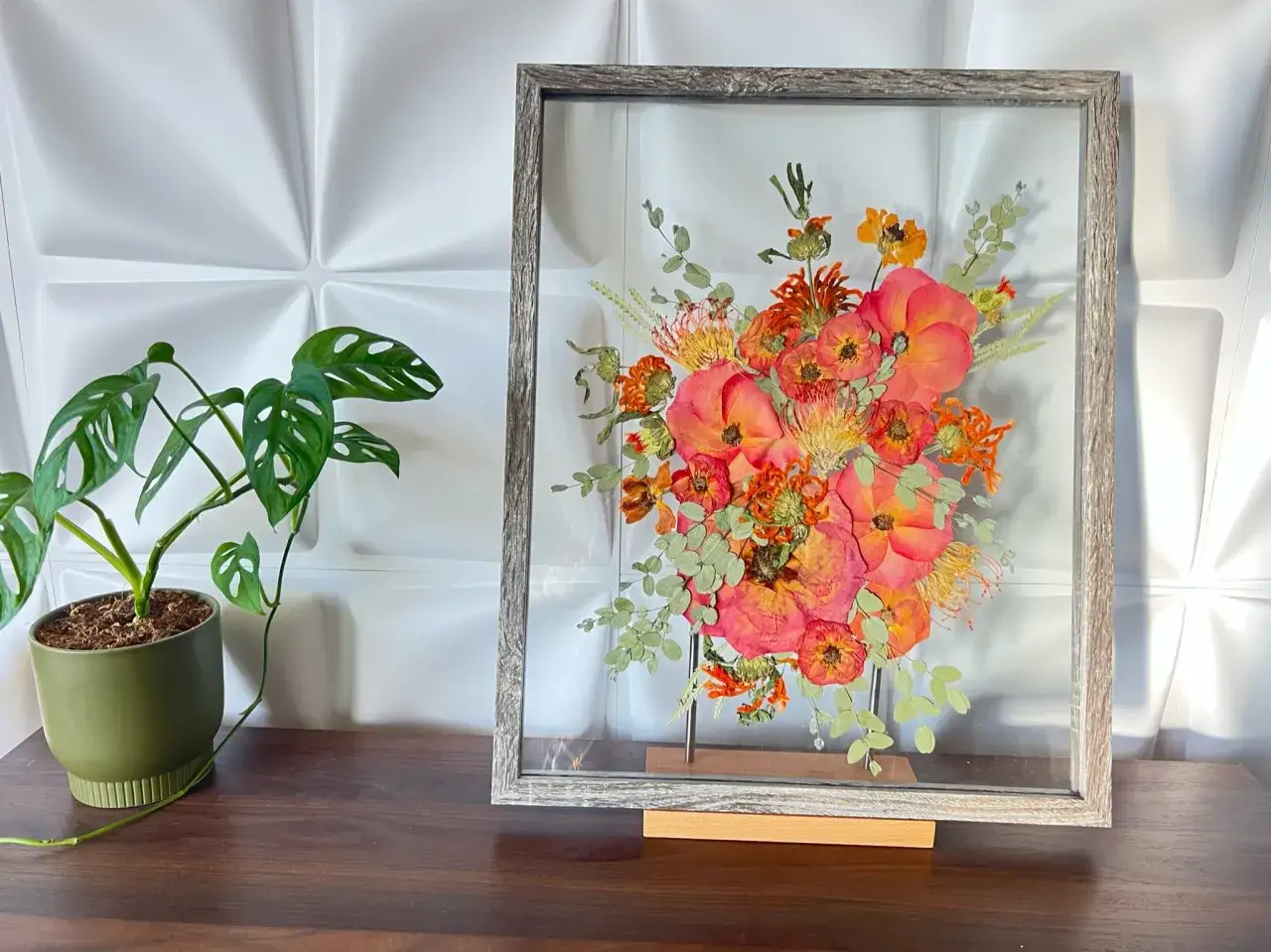 Cadre en bois gris contenant un bouquet de fleurs s&eacute;ch&eacute;es aux tons orang&eacute;s et roses. Une belle fa&ccedil;on de conserver le souvenir de fleurs cultiv&eacute;es pour les s&eacute;cher.