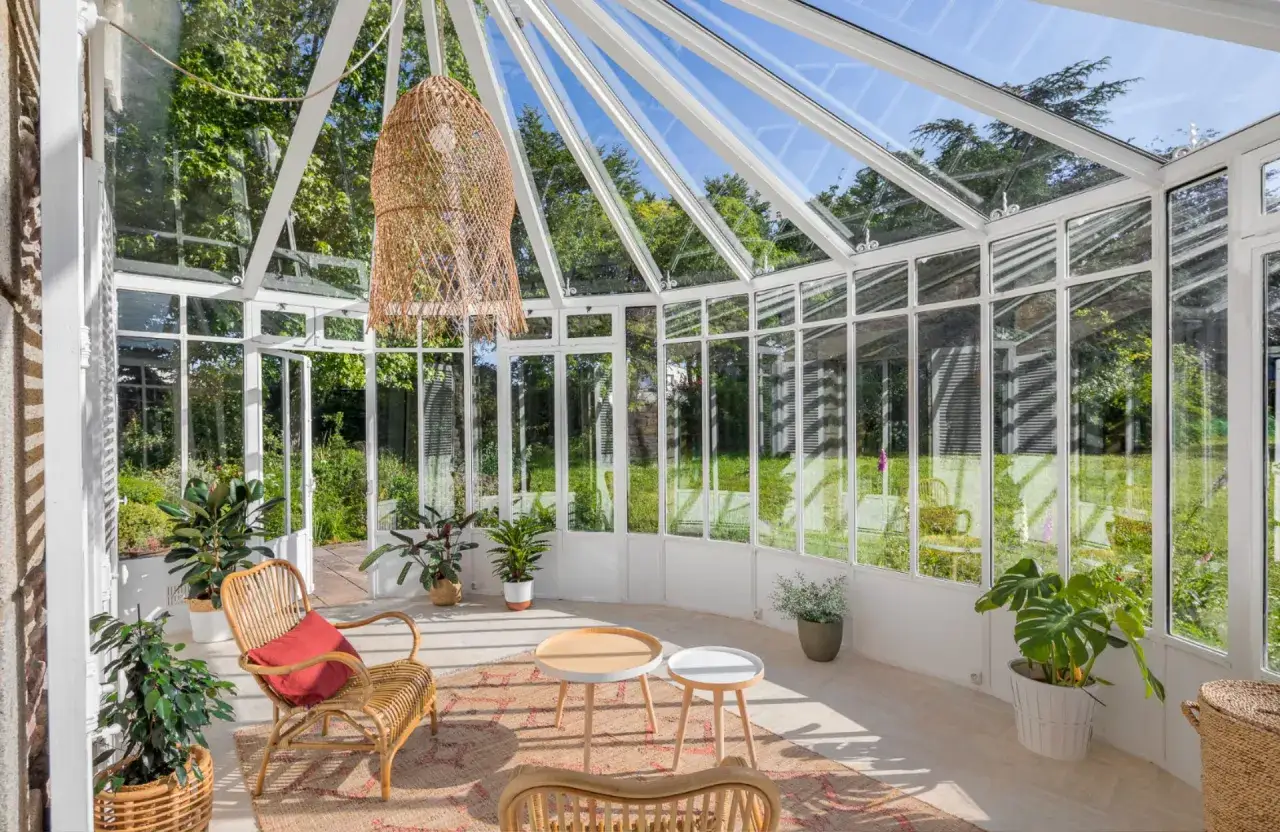 Un bel am&eacute;nagement de v&eacute;randa baign&eacute; de lumi&egrave;re, avec des meubles en rotin, des plantes vertes et une vue sur le jardin.