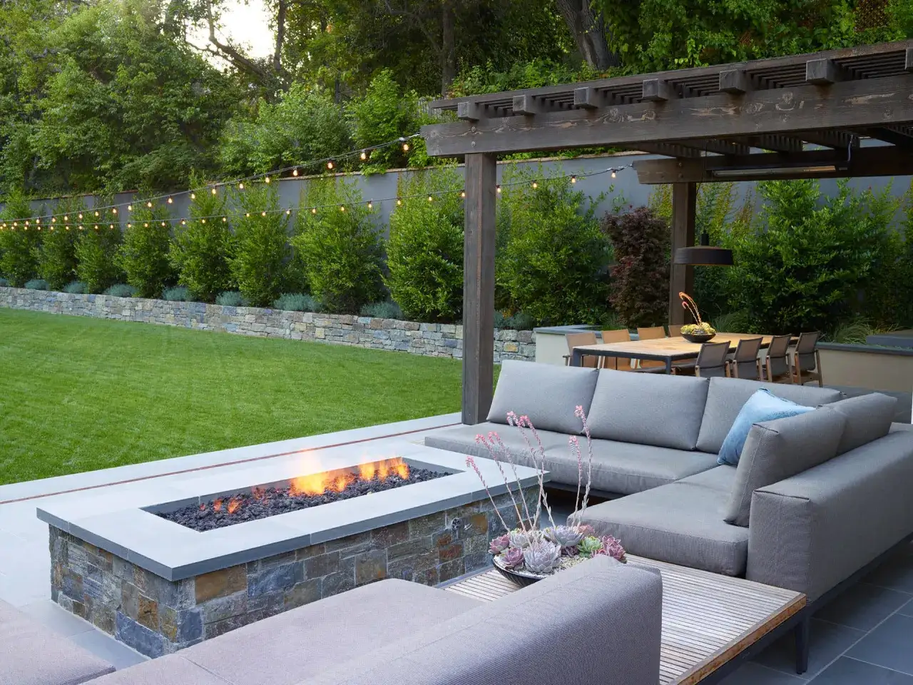Am&eacute;nagement terrasse ext&eacute;rieure avec un feu de camp, un salon confortable et une table &agrave; manger sous une pergola.